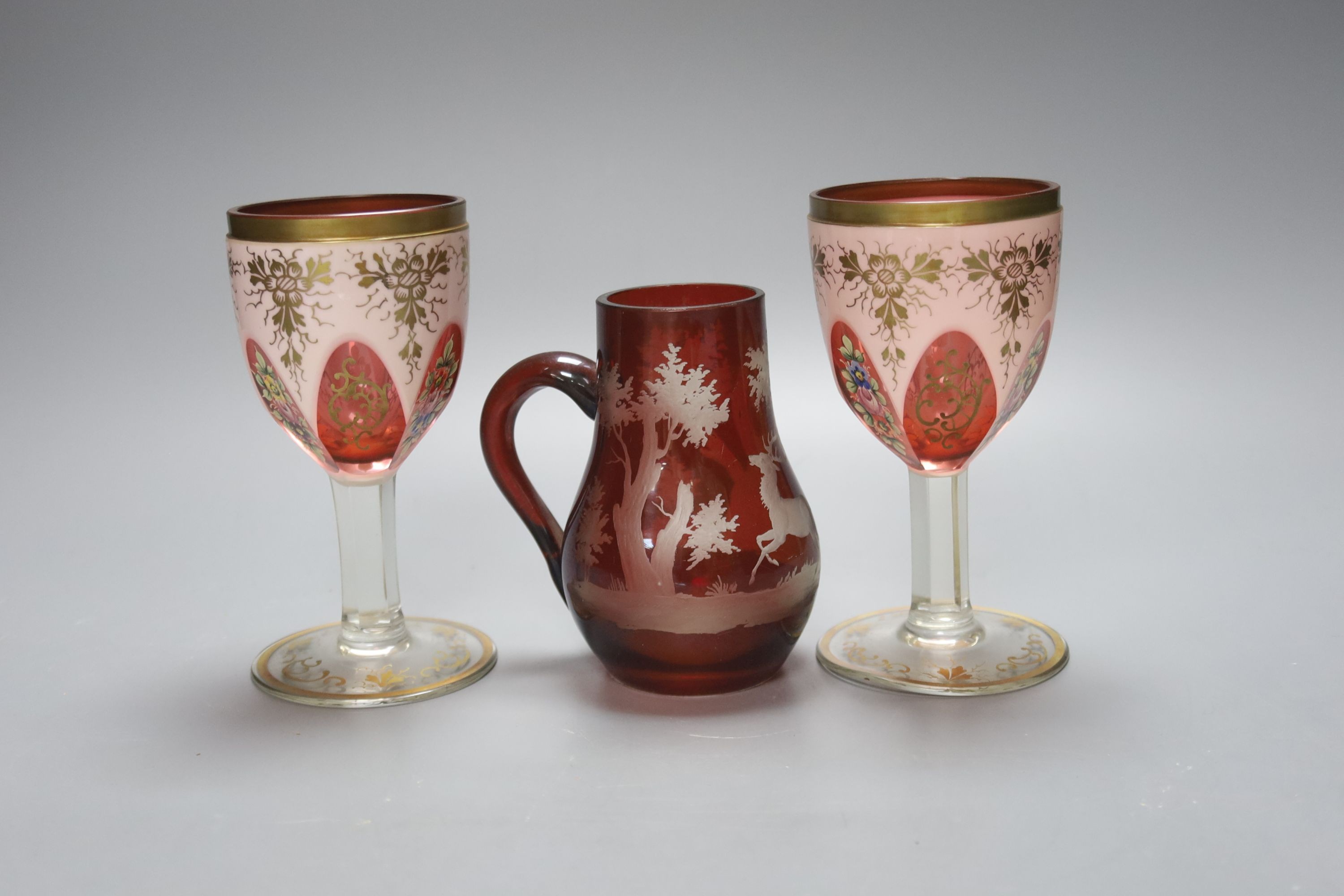 A pair of Bohemian overlaid glass goblets and a wheel engraved ruby glass jug (3) 15cm